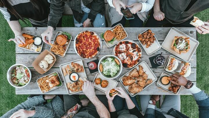 bird's eye view of a picnic table with all sorts of lunch options and 8 people sitting, talking, eating