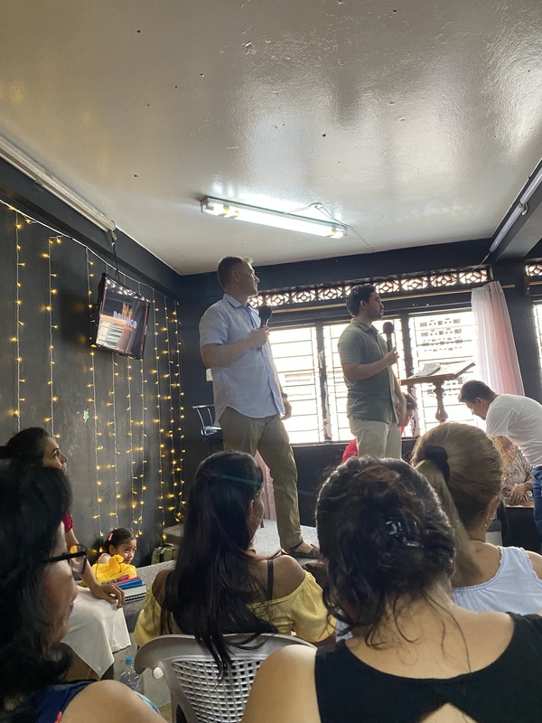 two people speaking on a stage to a group of kids