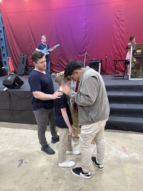 Two men praying over a boy in front of a stage at a worship meeting