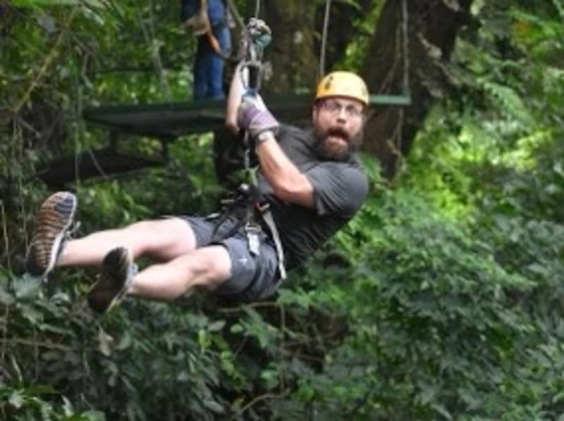 A man on a zip line wearing a yellow helmet, hanging in the el salvadoran forest