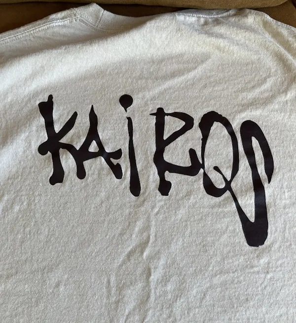 Kairos spray paint style on the back of a light sand tee